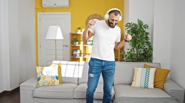 Genç İspanyol adam evde dans dinlerken kendinden emin bir şekilde gülümsüyor.