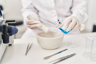 Young beautiful hispanic woman scientist pouring liquid on bowl at laboratory