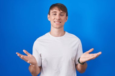 Mavi arka planda duran beyaz tenli sarışın adam gülümseyen, yardım eli uzatan ve kabul eden.. 