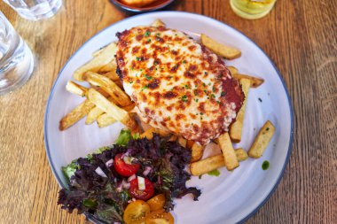  Lezzetli bir tabak İtalyan lazanyası kızarmış patates ve salata ahşap yüzeyi.