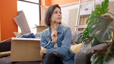 Kanepede oturan genç beyaz kadın yeni evinde yorgun olduğunu düşünüyor.