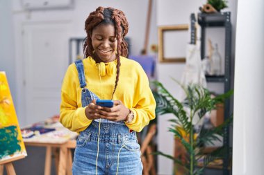 African american woman artist using smartphone standing at art studio