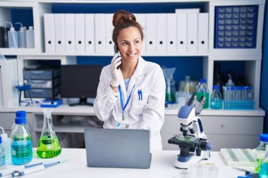 Young woman scientist talking on the smartphone using laptop at laboratory