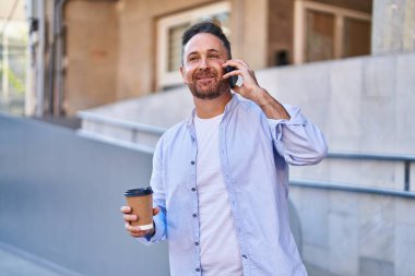 Young caucasian man talking on the smartphone drinking coffee at street