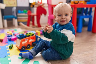 Beyaz tenli sevimli bir çocuk anaokulunda yerde oturmuş oyuncaklarla oynuyor.