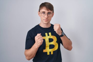 Beyaz, sarışın, Bitcoin tişörtlü adam. Yumruk savunma hareketleriyle dövüşmeye hazır. Kızgın ve üzgün. 