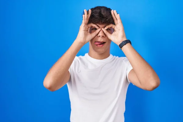 Hispanic Teenager Standing Blue Background Doing Gesture Binoculars Sticking Tongue — Stock Photo, Image