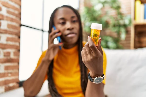 African American Woman Talking Smartphone Serious Expression Holding Pills Home — Stockfoto