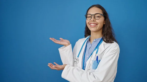 Młoda Piękna Latynoska Lekarz Uśmiecha Się Pewnie Prezentując Odizolowanym Niebieskim — Zdjęcie stockowe