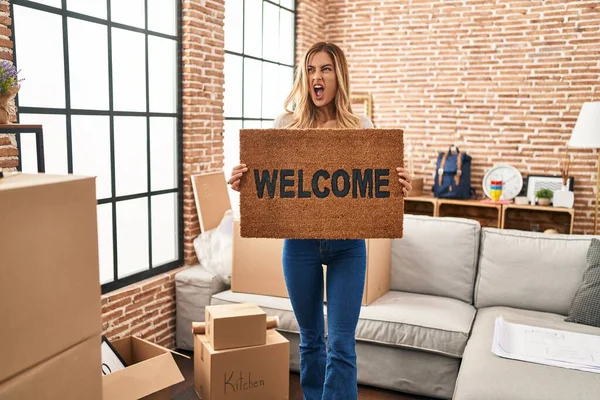 Young Blonde Woman Holding Welcome Doormat New Home Angry Mad — Stock Photo, Image