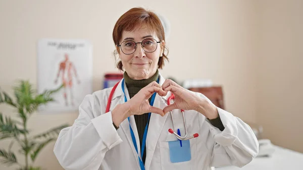 成熟的惊慌失措的女医生微笑着在诊所用手做心脏手势 — 图库照片