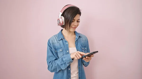 孤立したピンクの背景にヘッドフォンを身に着けているスマートフォンを使用して若い白人女性 — ストック写真