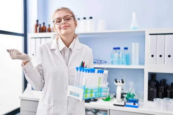 stock image Young caucasian woman working at scientist laboratory holding samples screaming proud, celebrating victory and success very excited with raised arm 