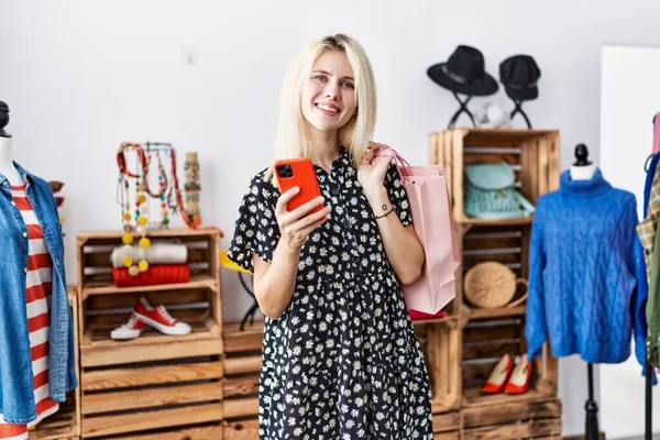 Joven Mujer Rubia Sosteniendo Bolsas Compras Usando Teléfono Inteligente Sonriendo —  Fotos de Stock