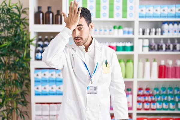 Homem Hispânico Bonito Trabalhando Farmácia Farmácia Surpreendido Com Mão Cabeça — Fotografia de Stock