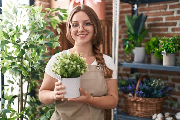Mulher Caucasiana Jovem Trabalhando Florista Loja Segurando Planta Olhando Positivo — Fotografia de Stock