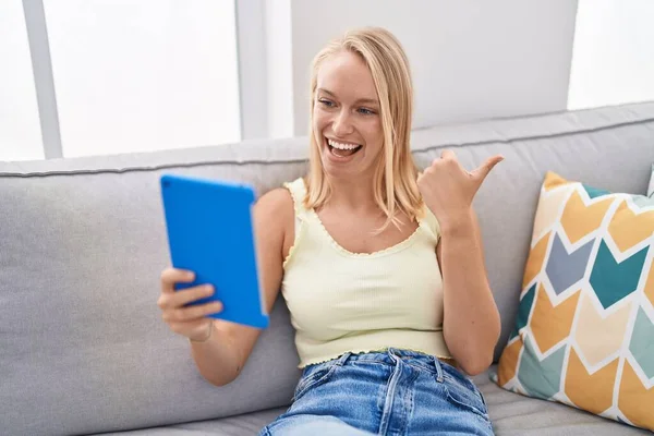 Young Caucasian Woman Using Touchpad Sitting Sofa Pointing Thumb Side — Stock Photo, Image