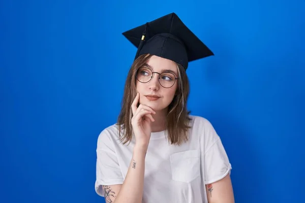 集中的な表現について考える顎の手で卒業キャップを身に着けているブロンドの白人女性 思慮深い顔で笑顔 疑わしい概念 — ストック写真