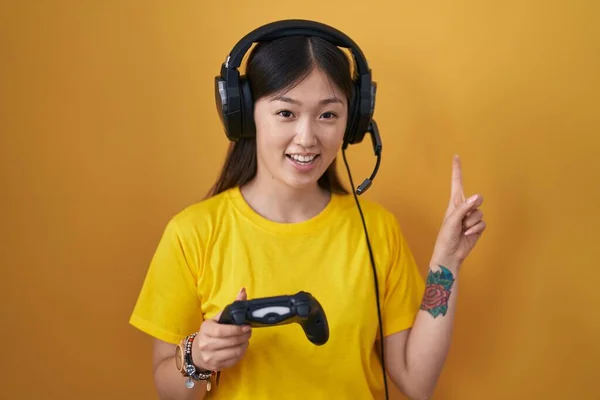 中国年轻女子拿着游戏控制器 脸上挂着大大的笑容 手指头指向旁边看相机 — 图库照片