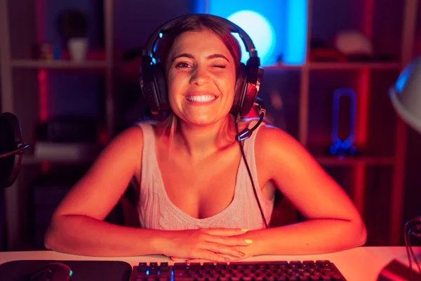 年轻的金发女人带着耳机玩电子游戏 带着性感的表情 快乐的面庞看着摄像机眨眼 — 图库照片