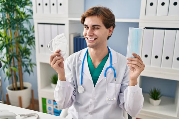 Young Doctor Man Holding Two Safety Mask Winking Looking Camera — Stock Photo, Image