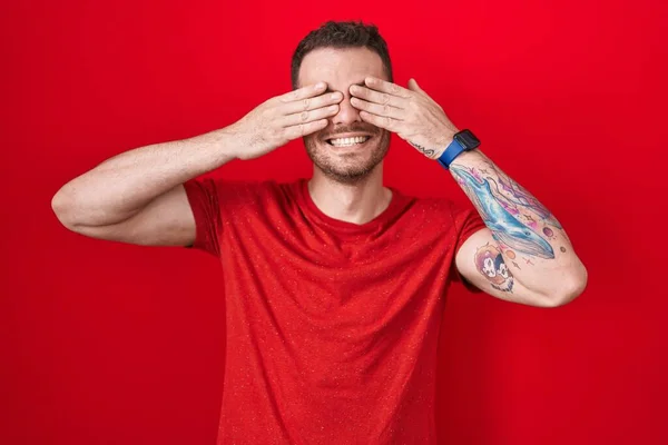 Young Hispanic Man Standing Red Background Covering Eyes Hands Smiling — Stockfoto