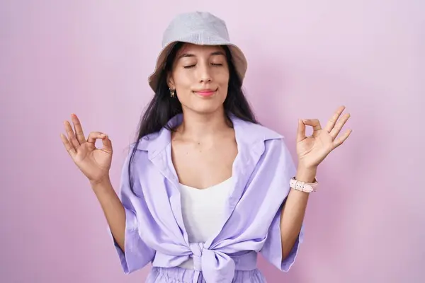 ピンクの背景の上に立つ若いヒスパニック系の女性は 指で瞑想のジェスチャーを行う目でリラックスして笑顔を着ています ヨガのコンセプト — ストック写真