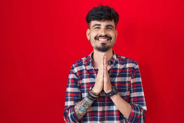 Mladý Hispánec Plnovousem Stojící Nad Červeným Pozadím Modlí Rukama Sobě — Stock fotografie