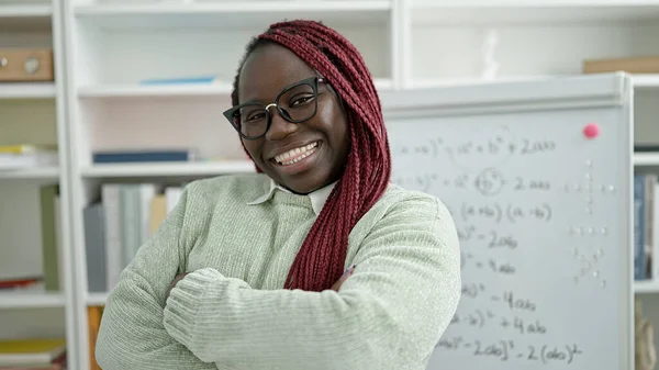 African woman with braided hair standing by white board smiling at university library