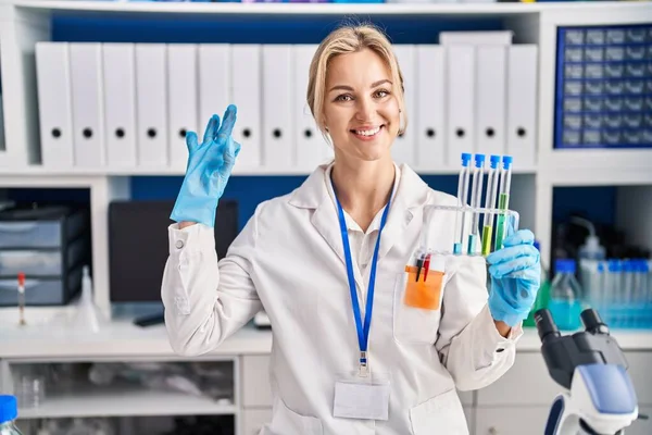 과학자 실험실에서 테스트 튜브를 손가락으로 보이는 사인을 친절하게 미소짓는 미소를 — 스톡 사진
