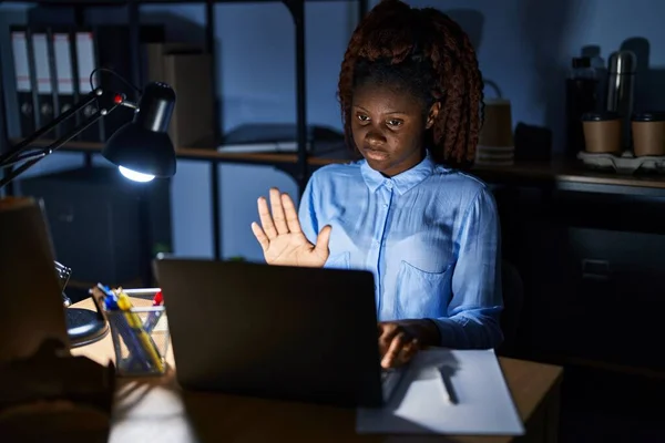 African woman working at the office at night doing stop sing with palm of the hand. warning expression with negative and serious gesture on the face.