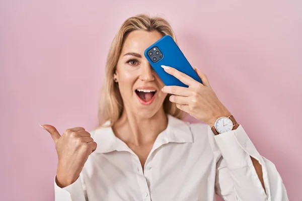 Mujer Joven Caucásica Cubriendo Ojo Con Teléfono Inteligente Apuntando Pulgar —  Fotos de Stock