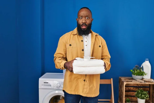 Africký Američan Drží Čisté Ručníky Prádelně Šoku Tvář Vypadá Skeptický — Stock fotografie