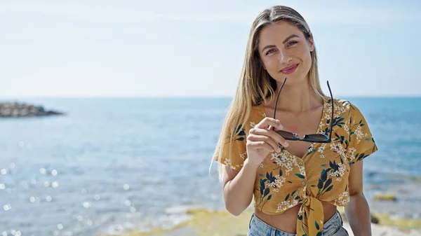 Joven Mujer Rubia Sonriendo Confiada Sosteniendo Gafas Sol Playa —  Fotos de Stock