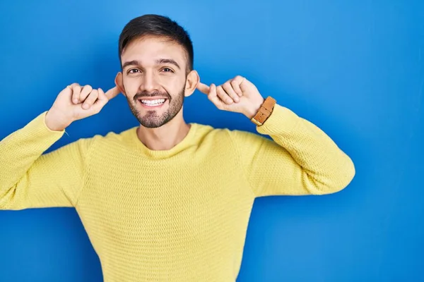 Spanischer Mann Vor Blauem Hintergrund Lächelnd Mit Fingern Ohren Zuziehend — Stockfoto