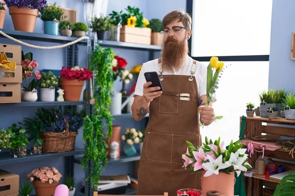 Młody Ruda Mężczyzna Kwiaciarnia Pomocą Smartfon Gospodarstwa Kwiat Kwiaciarnia — Zdjęcie stockowe