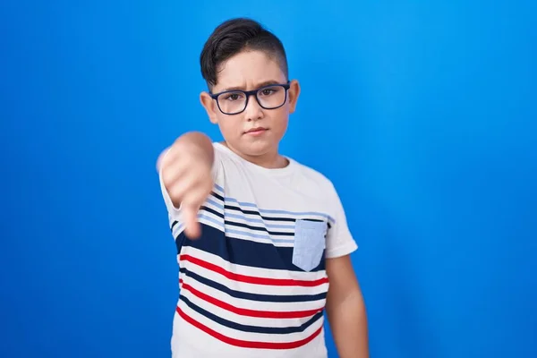 青の背景に立っている若いヒスパニック系の子供は 親指を下にジェスチャーで拒絶と否定を示す不満と怒りを見ています 悪い表現 — ストック写真