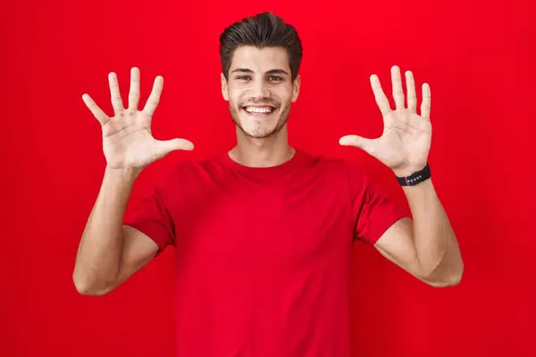 年轻的他的惊慌失措的男人站在红色的背景上 用十号手指指指着 自信而快乐地微笑着 — 图库照片