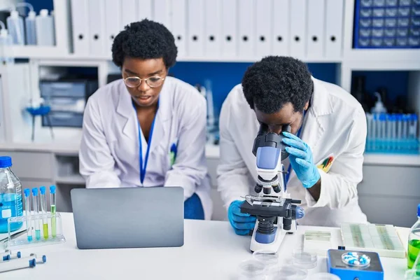 アフリカ系アメリカ人の男性と女性の科学者が実験室でノートパソコンと顕微鏡を使って — ストック写真