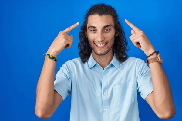 Joven Hombre Hispano Pie Sobre Fondo Azul Sonriendo Señalando Cabeza — Foto de Stock