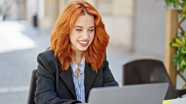 年轻的红头发女商人在咖啡店的阳台上微笑着使用笔记本电脑 — 图库照片