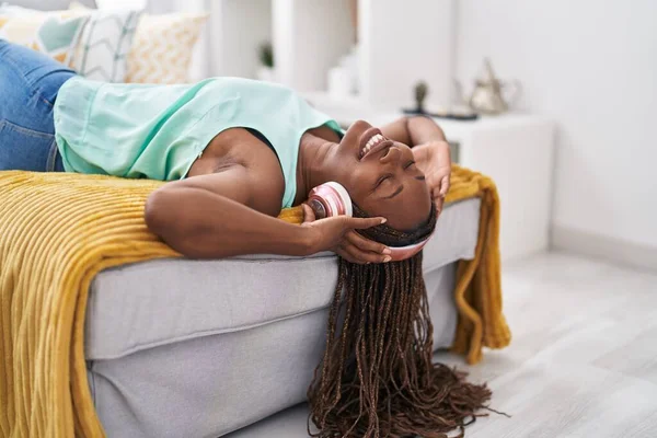 听音乐的非洲裔美国妇女躺在家里的沙发上 — 图库照片