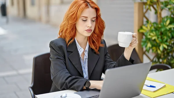 年轻的红头发女商人在咖啡店的阳台上用笔记本电脑喝咖啡 — 图库照片