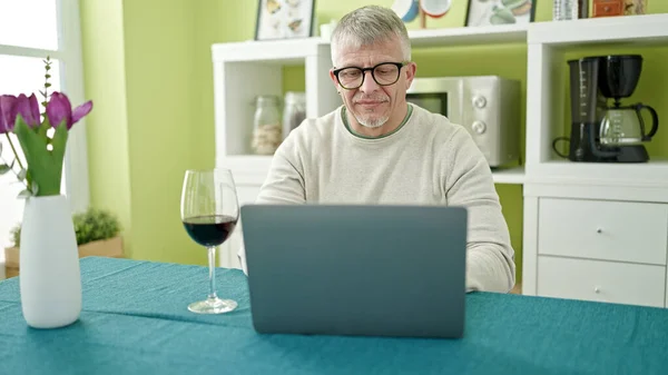 中世の白髪の男自宅でノートパソコンを使用してワインのグラスを飲む — ストック写真