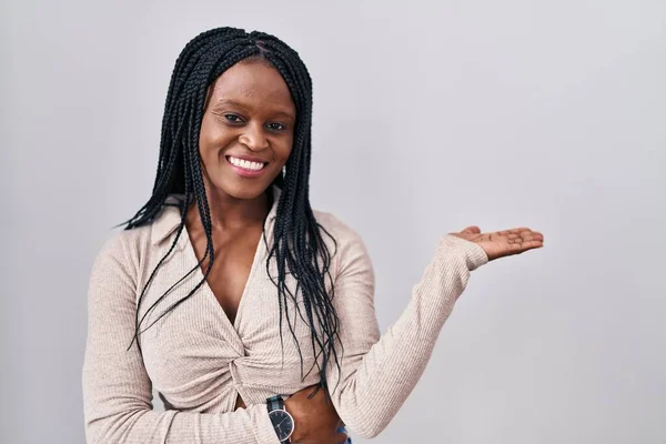 白い背景の上に立っているアフリカの女性笑顔陽気に提示し カメラを見て手の手のひらで指しています — ストック写真