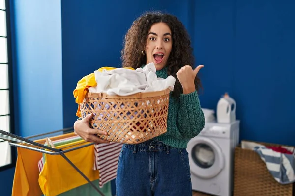 Ung Latinamerikansk Kvinna Håller Tvättkorg Pekar Tumme Upp Till Sidan — Stockfoto