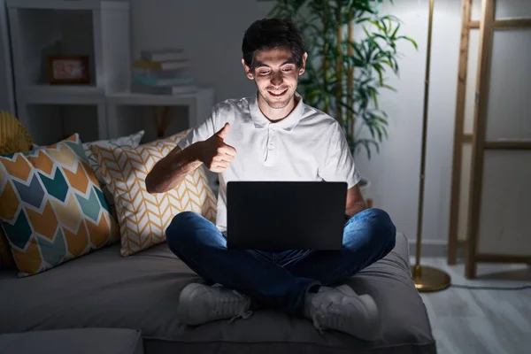 夜に自宅でラップトップを使用している若いヒスパニック系の男性は 手で積極的なジェスチャーを行うことを承認します 親指アップ笑顔と成功のために幸せ 勝者のジェスチャー — ストック写真