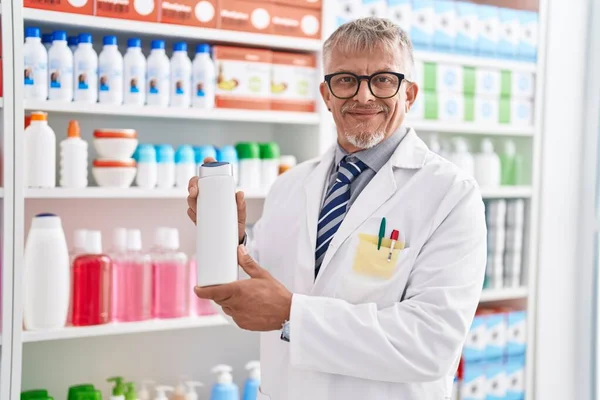 研究室でシャンプーボトルを保持している中年白髪の男性薬剤師 — ストック写真
