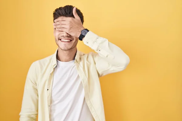 Mladý Hispánec Stojící Nad Žlutým Pozadím Usmívající Rukou Tváři Zakrývající — Stock fotografie