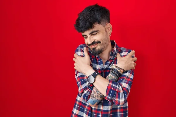 Mladý Hispánec Plnovousem Stojící Nad Červeným Pozadím Objímající Šťastný Pozitivní — Stock fotografie